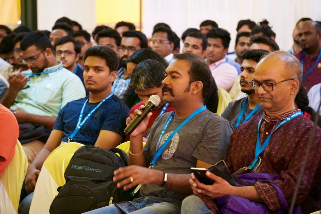 A group of people listening to a session, and a man with a mic asking a question at WordCamp Kochi 2017. 